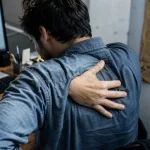 Douleurs dorsales signification : main sur le haut du dos au bureau
